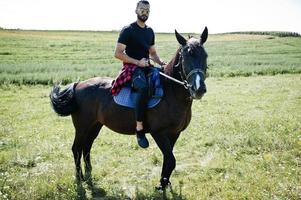 barbe haute arabe homme porter en noir et lunettes de soleil ride cheval arabe. photo