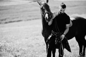 homme arabe à barbe haute en noir avec cheval arabe. photo