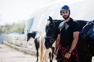 l'homme arabe à grande barbe porte un casque noir avec un cheval arabe. photo
