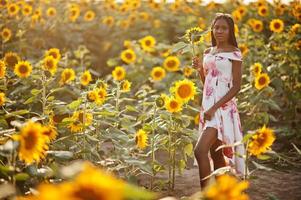 jolie jeune femme noire porte une robe d'été pose dans un champ de tournesol. photo