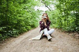 portrait d'une jolie fille blonde avec une carte assise dans la forêt et prenant des photos. photo