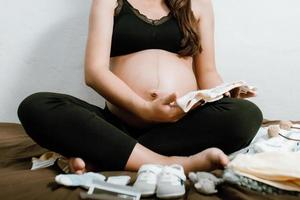 femme enceinte tenant un body bébé dans la chambre avec un jouet et les nécessités pour l'accouchement du nouveau-né. femme enceinte attendant et se préparant à la naissance du bébé. notion de femme enceinte. photo