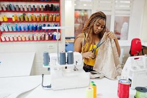 une jeune couturière africaine coud des vêtements sur une machine à coudre et utilise des ciseaux au bureau de tailleur. femmes couturières noires. photo
