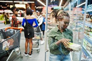 groupe de femmes africaines avec des caddies près de l'étagère du réfrigérateur vendant des cartons d'oeufs de produits laitiers dans le supermarché. photo
