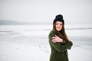 fille drôle portant un long sweat-shirt vert, un jean et un couvre-chef noir, au lac gelé en hiver. photo