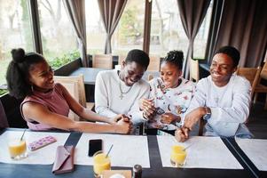 amis africains heureux assis et bavardant au café. groupe de peuples noirs se rencontrant et jouant à des jeux à la main au restaurant. photo