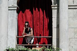 élégante femme afro-américaine posée au balcon avec rideau rouge en plein air. photo