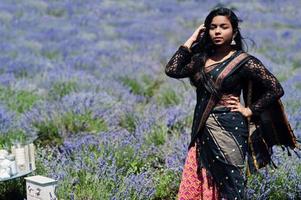 belle fille indienne porte une robe traditionnelle indienne saree dans un champ de lavande violette. photo