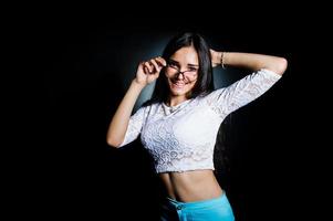 portrait d'une jolie jeune femme en haut blanc et pantalon bleu posant avec ses lunettes dans le noir. photo