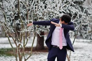 élégant modèle d'homme macho indien en costume et cravate rose, lunettes de soleil posées le jour de l'hiver montre dab. photo