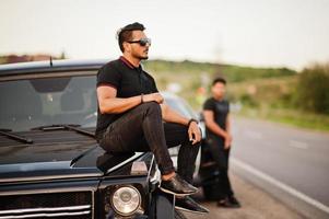deux frères asiatiques portent un homme tout noir posé près de voitures suv. photo