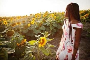 jolie jeune femme noire porte une robe d'été pose dans un champ de tournesol. photo