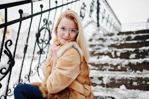 portrait d'une fille blonde à lunettes, manteau de fourrure rouge et écharpe le jour de l'hiver. photo