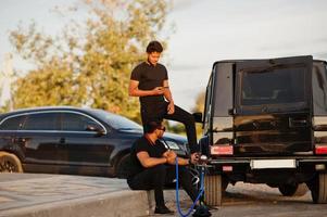 deux frères asiatiques portent un homme tout noir posé près de voitures suv et fument le narguilé. photo