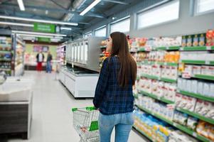 femme commerçante regardant les étagères du supermarché avec panier. portrait d'une jeune fille dans un magasin de marché. photo