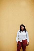 femme d'affaires afro-américaine formellement habillée en chemisier blanc et pantalon rouge isolé sur fond jaune. femme d'affaires prospère à la peau foncée. photo