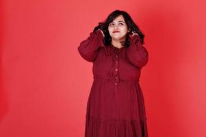 jolie femme sud-asiatique en robe rouge foncé posée au studio sur fond rose. photo