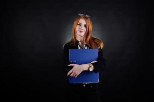 portrait d'une femme d'affaires rousse portant un chemisier rayé, des lunettes et une veste avec un dossier bleu. photo