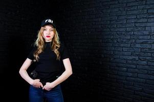 agent féminin du fbi en casquette et avec arme à feu au studio contre un mur de briques sombres. photo