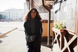 fille afro-américaine élégante en manteau bleu et lunettes de soleil posées à la journée d'automne ensoleillée. femme modèle afrique. photo