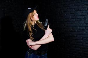 agent féminin du fbi en casquette et avec arme à feu au studio contre un mur de briques sombres. photo