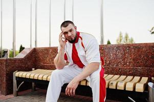 jeune homme musclé barbu brutal porte un costume de sport blanc avec une chemise rouge. photo