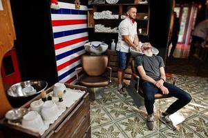 jeune homme barbu se lavant la tête par le coiffeur alors qu'il était assis sur une chaise au salon de coiffure. âme de barbier. photo