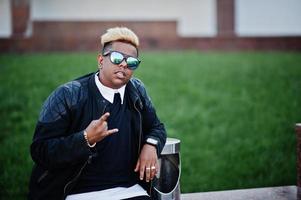 garçon musulman arabe élégant avec à l'origine des cheveux et des lunettes de soleil posés dans les rues, assis sur un banc. photo