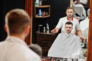 jeune homme barbu se coupe les cheveux par un coiffeur assis sur une chaise au salon de coiffure. âme de barbier. photo