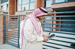 homme arabe du moyen-orient posé dans la rue contre un bâtiment moderne avec une tablette à portée de main. photo