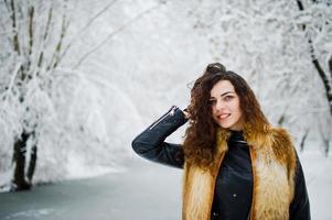 élégance bouclée fille en manteau de fourrure au parc forestier enneigé en hiver. photo