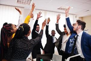 des hommes d'affaires multiraciaux debout au bureau et levant les mains. groupe diversifié d'employés en tenue de soirée. photo