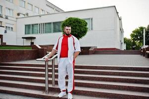 jeune homme musclé barbu brutal porte un costume de sport blanc avec une chemise rouge. photo