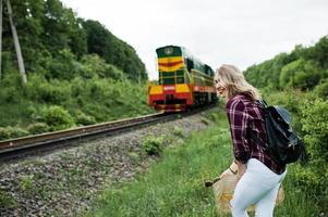 portrait d'une jeune blonde en chemise tartan à côté du train avec une carte. photo