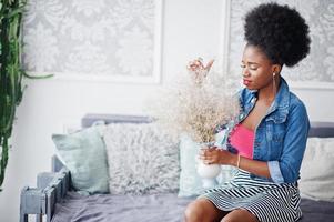 jolie femme afro-américaine aux cheveux afro portant une jupe et une veste en jean, posée dans la salle blanche. modèle noir à la mode. photo