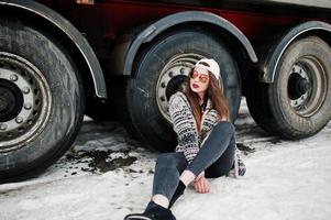 brune élégante fille décontractée en casquette et lunettes de soleil assise contre les roues du camion. photo