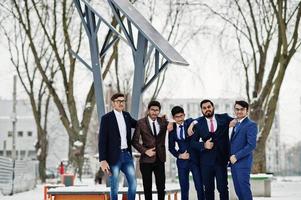 groupe de cinq hommes d'affaires indiens en costumes posés à l'extérieur en journée d'hiver en europe contre des panneaux solaires. photo