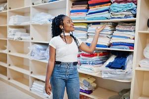 une femme afro-américaine joyeuse se tient près des étagères avec des serviettes dans la blanchisserie en libre-service. photo