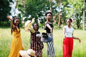 groupe de quatre magnifiques femmes afro-américaines portant un chapeau d'été passant du temps à l'herbe verte dans le parc.