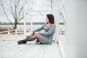 portrait de jeune fille brune en robe grise assis à la construction en bois blanc. photo