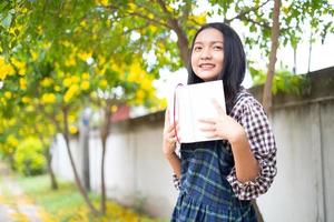 une jeune fille tient un livre et se tient sous un bel arbre. photo