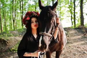 fille mystique en guirlande en noir avec cheval en bois. photo