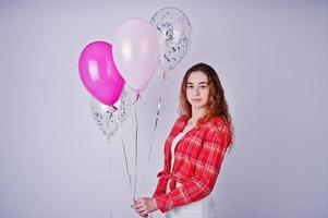 jeune fille en chemise à carreaux rouge et pantalon blanc avec des ballons sur fond blanc en studio. photo