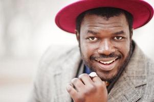 portrait en gros plan d'un élégant modèle d'homme afro-américain en manteau gris, cravate de veste et chapeau rouge. photo