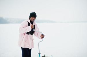 pêcheur afro-américain faisant un trou dans la glace gelée par forage. pêche d'hiver. photo