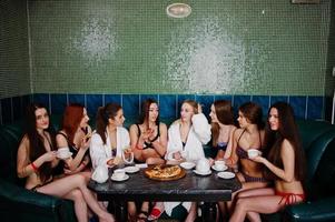 groupe de huit filles sexy en maillot de bain et peignoir assis dans un bain et mangeant de la pizza. les filles se reposent amies. photo