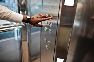 photo en gros plan de la main d'un homme afro-américain avec des montres à l'élévateur ou à l'ascenseur moderne, en appuyant sur le bouton.