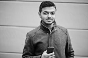 homme hindou indien élégant en manteau gris posé dans la rue avec un téléphone portable à portée de main. photo