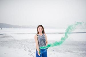 jeune fille avec une bombe fumigène de couleur verte à la main en journée d'hiver. photo