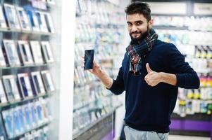 l'acheteur client de l'homme de barbe indien au magasin de téléphonie mobile choisit son nouveau smartphone et montre le pouce vers le haut. concept de peuples et de technologies d'asie du sud. magasin de téléphonie mobile. photo